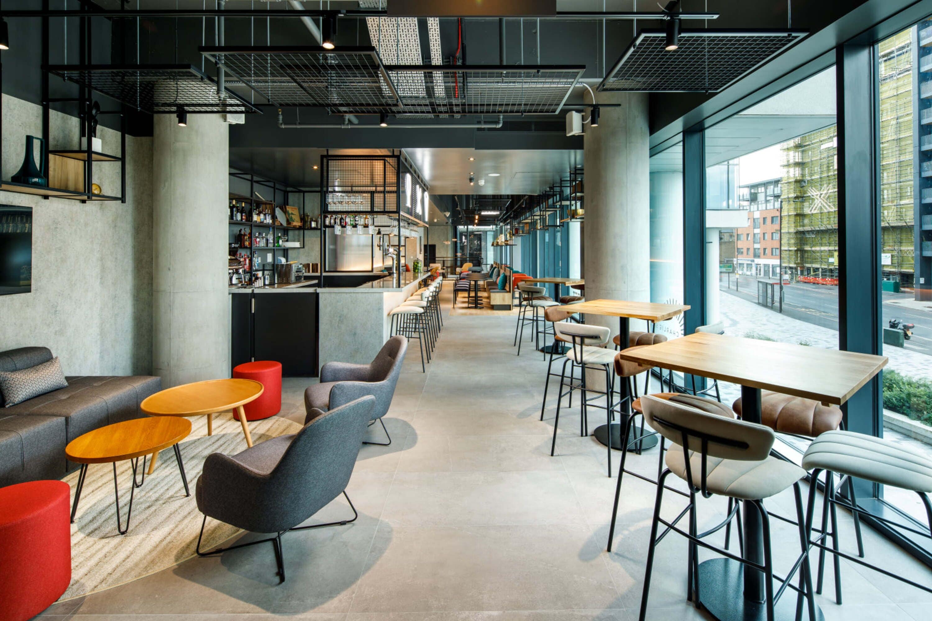 A modern cafe with a bar area, seating arrangements, and large windows offering a view of the street.