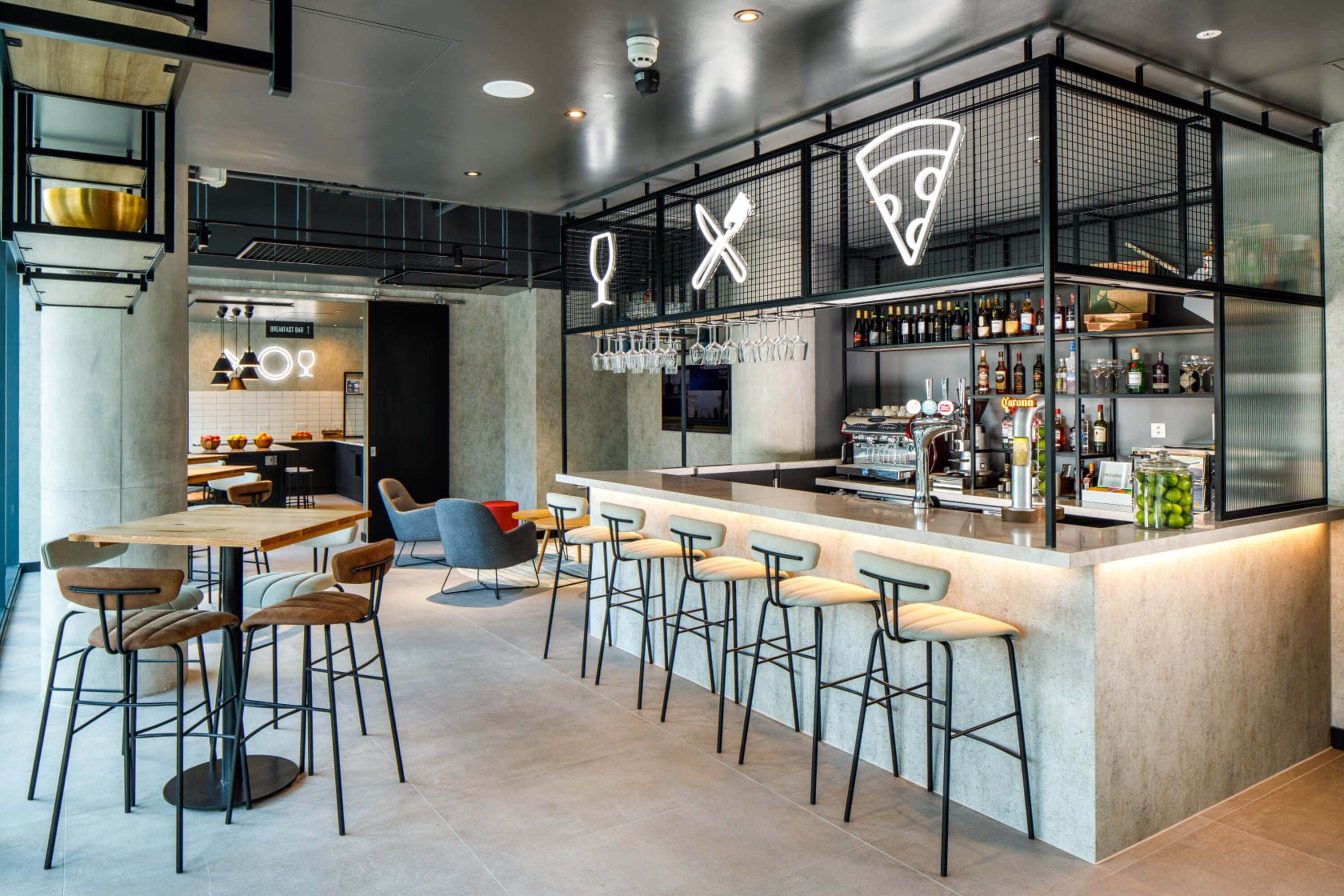 Un área de bar moderna con taburetes, una barra con botellas y un letrero de neón.