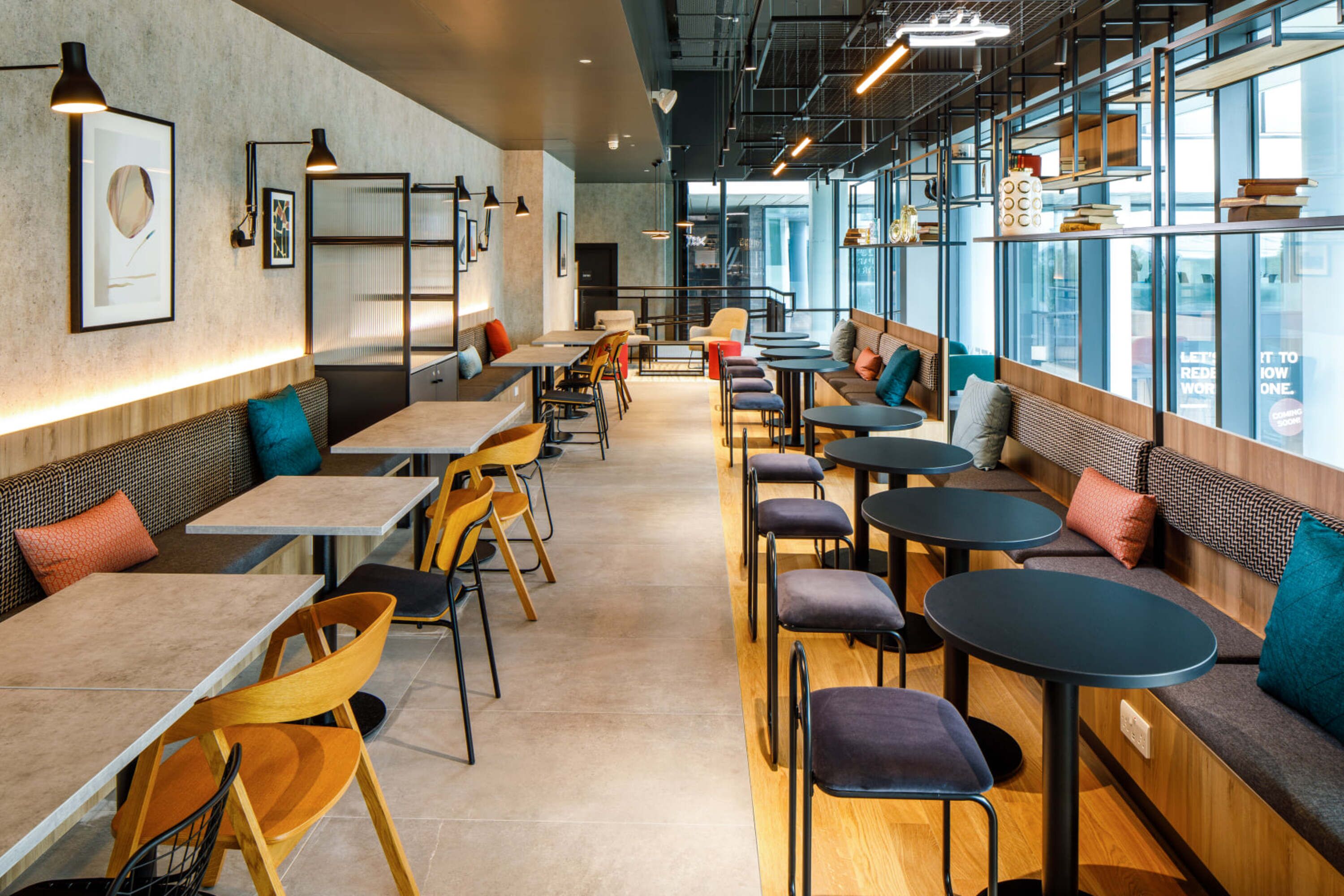 Um café moderno com mesas comunitárias alongadas, lugares individuais e janelas amplas com vista.