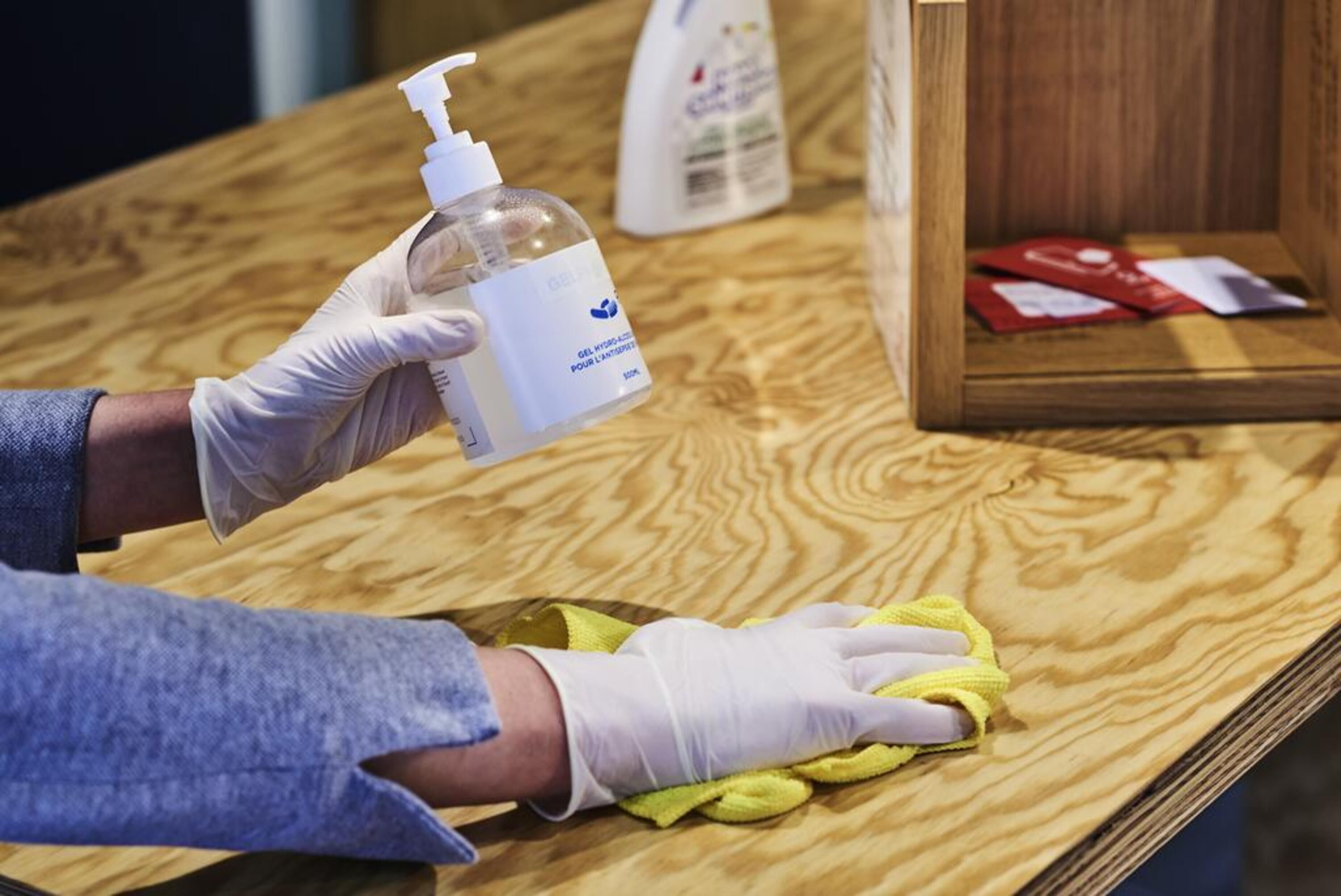 A person cleaning a wooden surface with a yellow cloth and a bottle of cleaning solution.