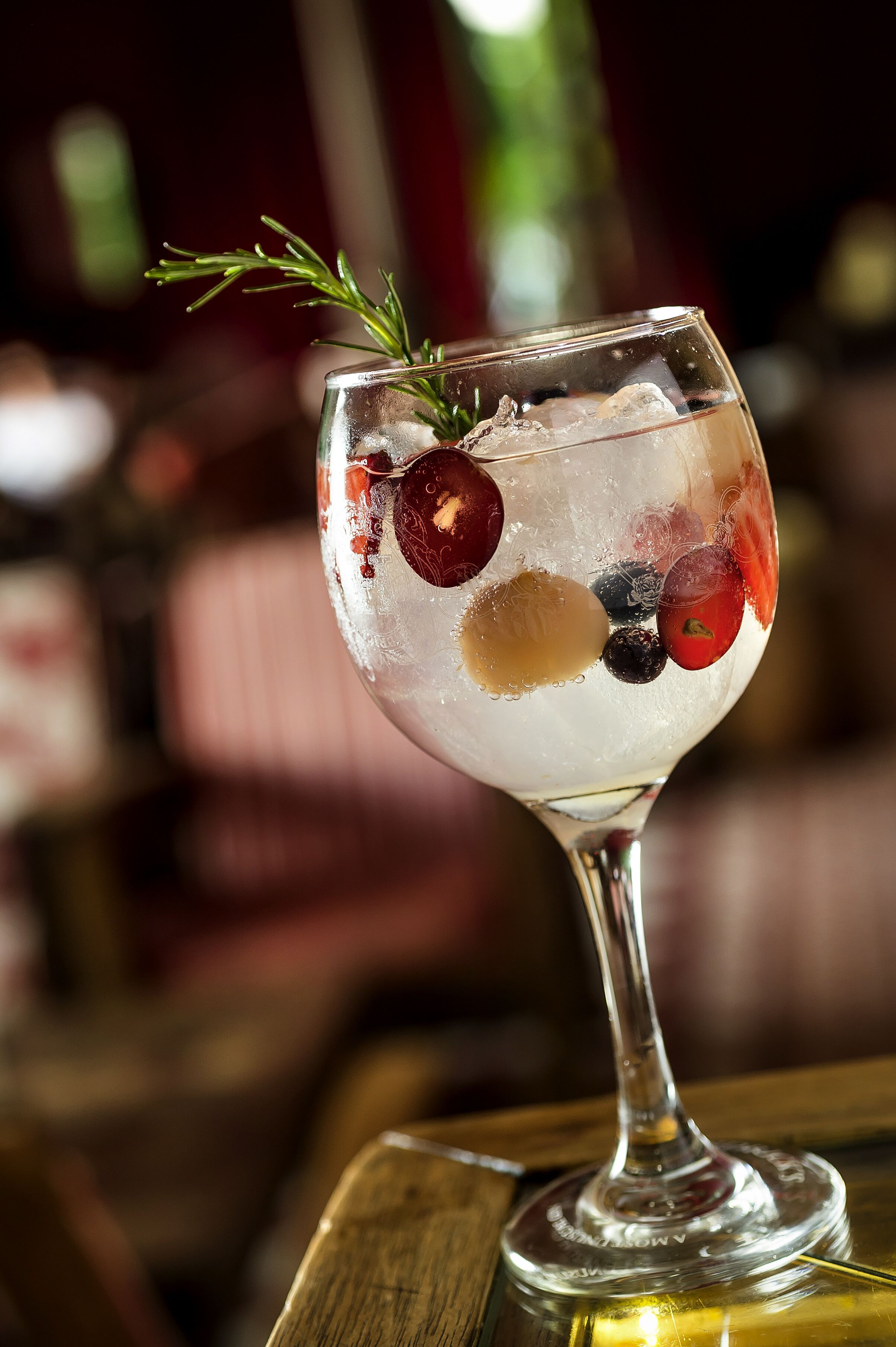 Un vaso de cóctel con hielo y fruta sobre una barra de madera.