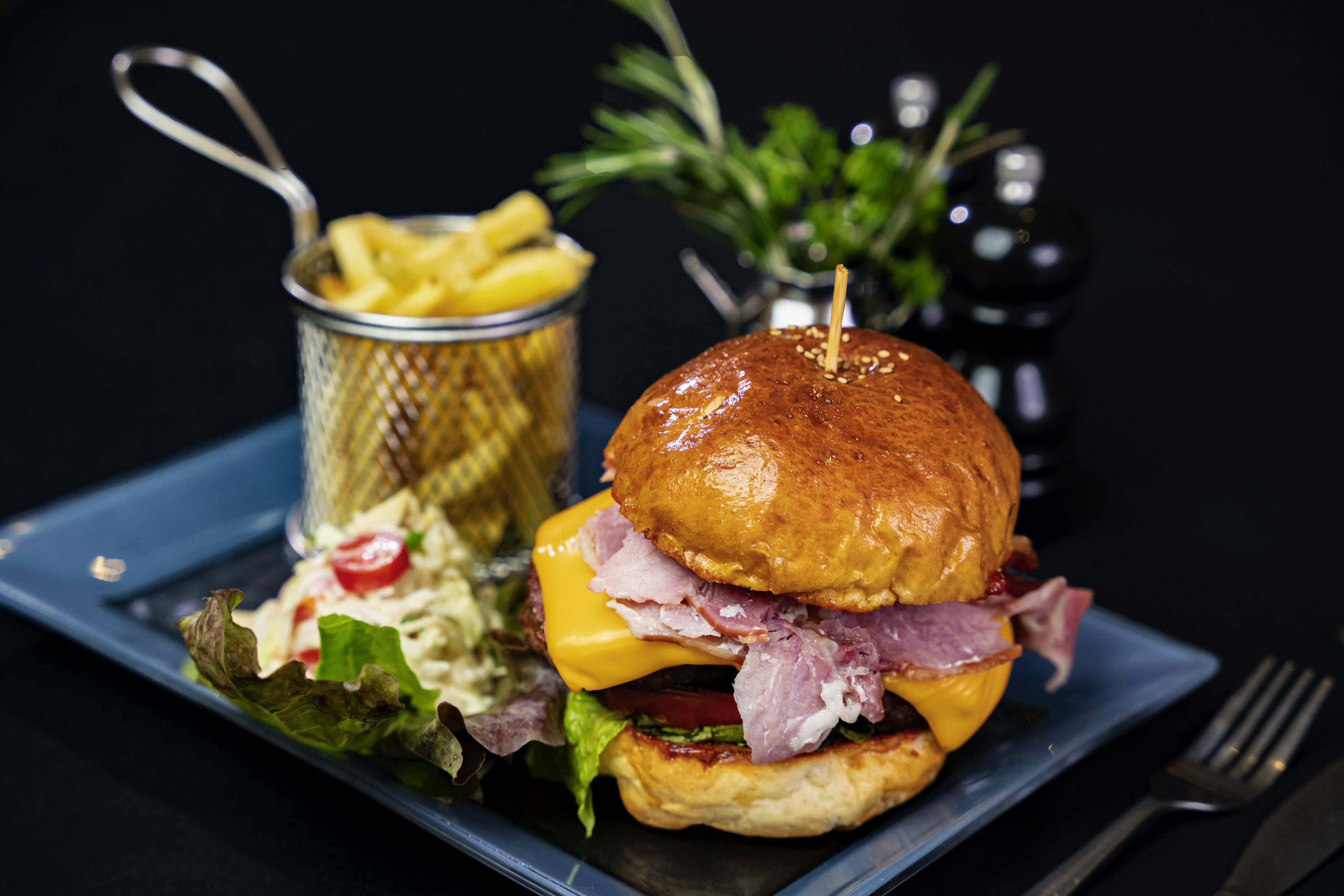 A sandwich with lettuce, tomato, cheese, and meat, accompanied by a side of fries and a small salad.