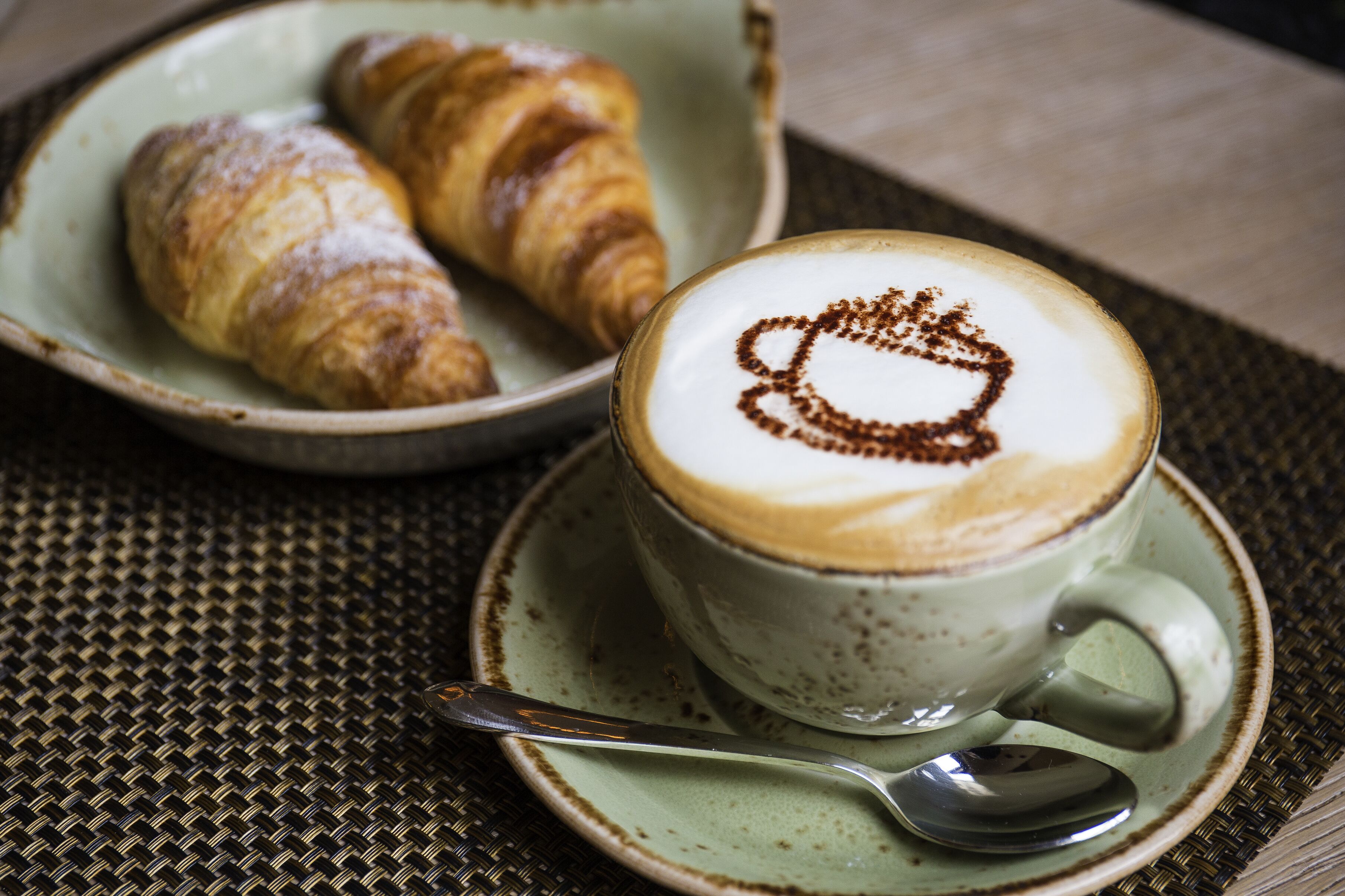 A cup of coffee with latte art and two croissants on a plate.