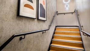 Eine Treppe mit Holzboden und Metallgeländern, die zu einer Wand mit abstrakter Kunst und einem Neonlicht führt.