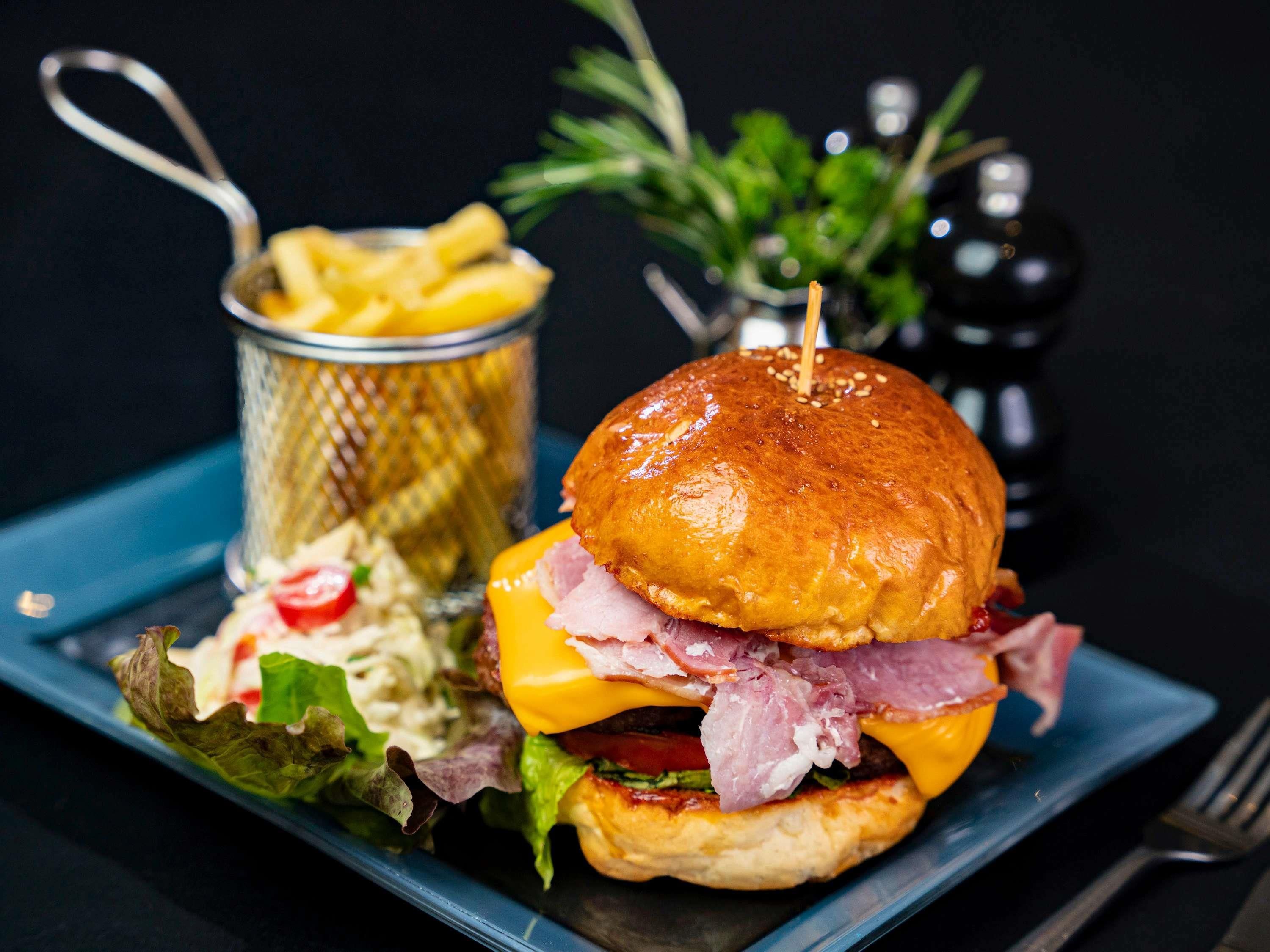 Ein Burger mit Salat, Tomate, Käse und Fleisch, dazu Pommes und ein Salat, serviert auf einem blauen Teller.