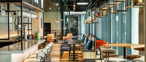 Una cafetería moderna con asientos de bar, mesas altas y una combinación de sillas y sofás.
