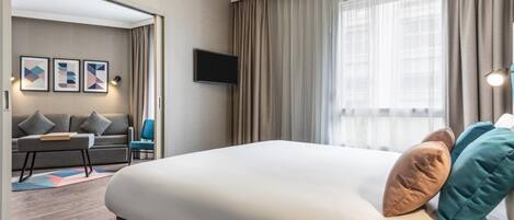 Una habitación de hotel con una cama grande, un televisor de pantalla plana en la pared, un sofá y una mesita.