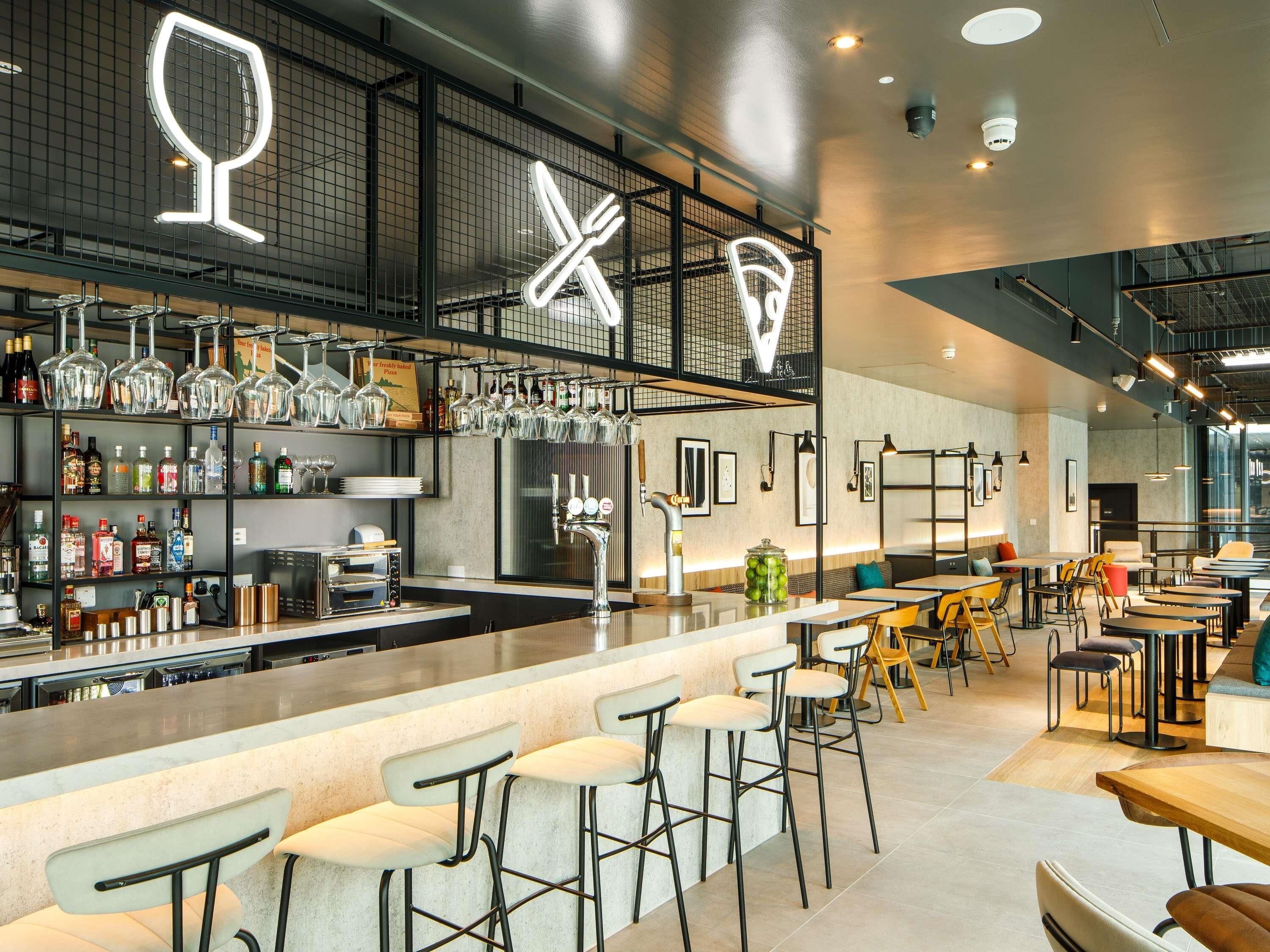 A modern bar area with a counter, stools, and a variety of bottles and glasses.