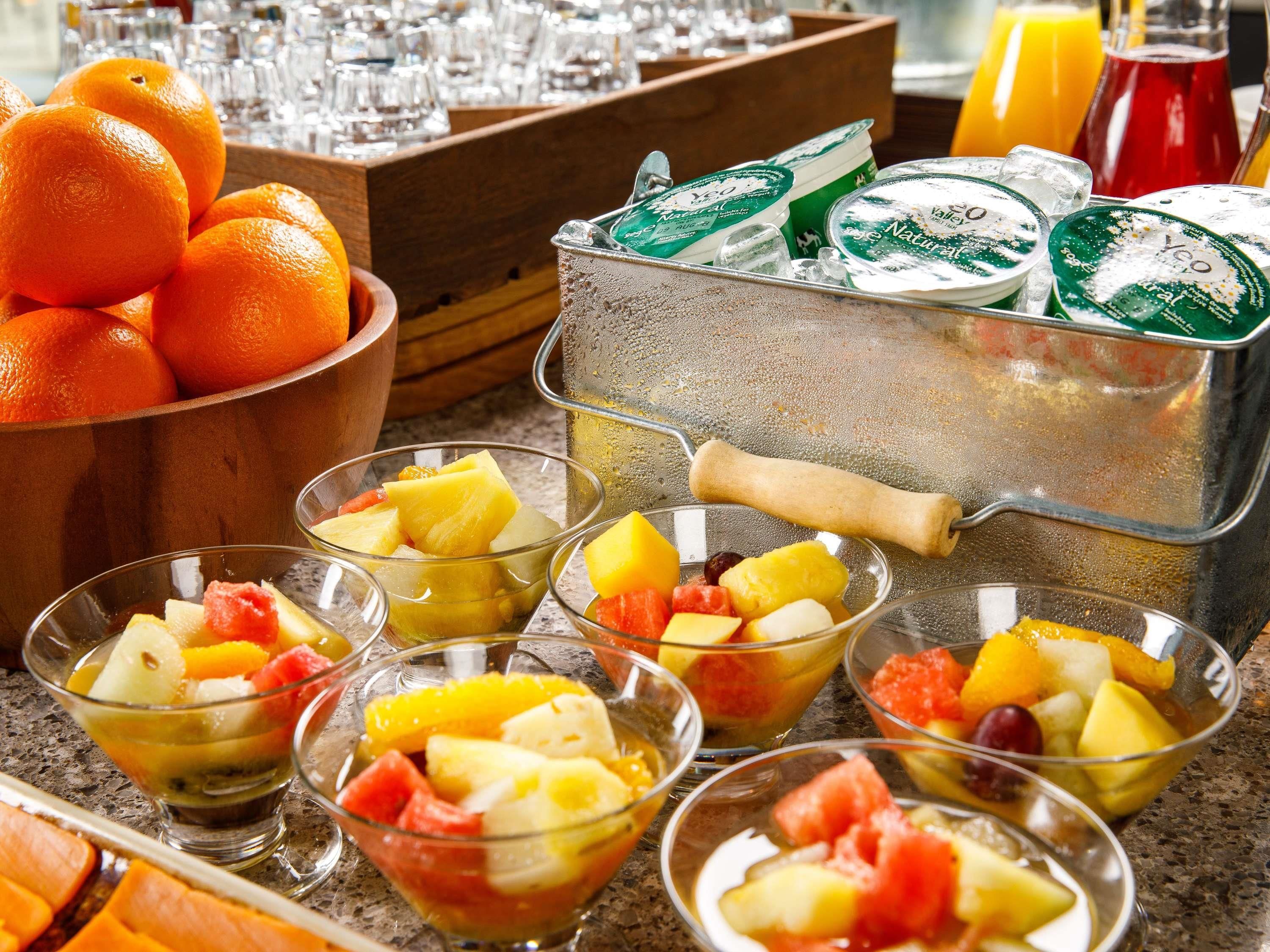 A buffet setup with fruit bowls, a fruit cooler, and a bowl of oranges.