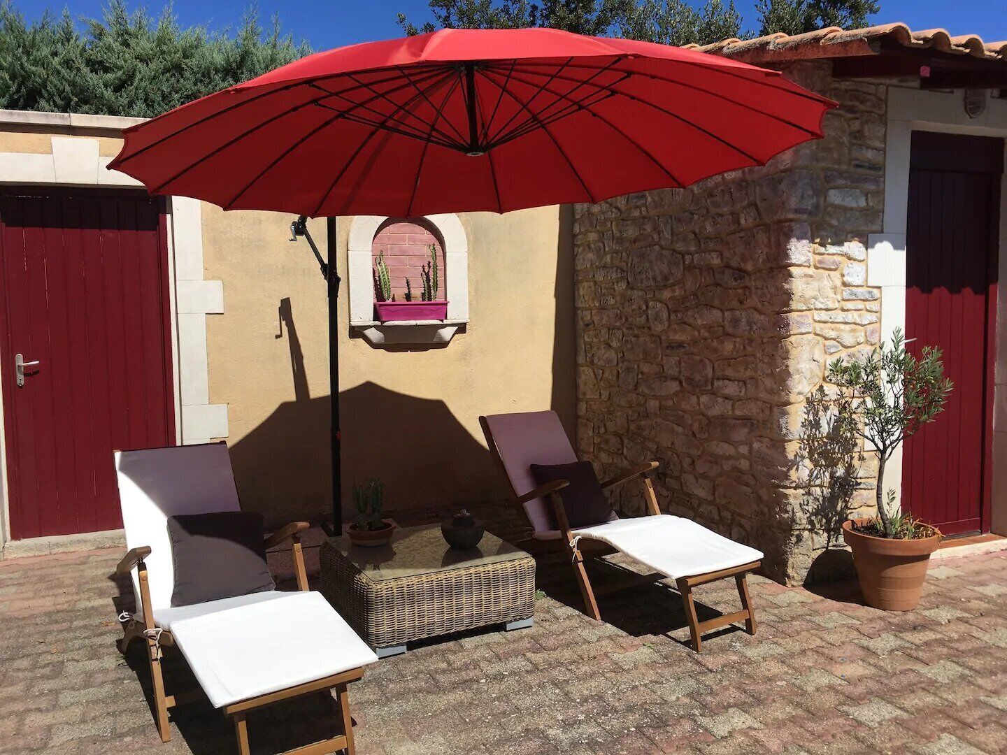 A patio with two lounge chairs, a red umbrella, and a small table.