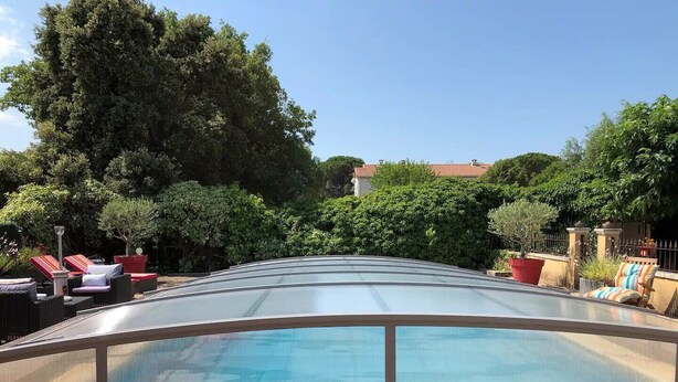 A swimming pool with a glass enclosure, surrounded by lounge chairs and potted plants.