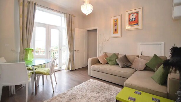 A living room with a beige sofa, a glass dining table, and a chandelier.