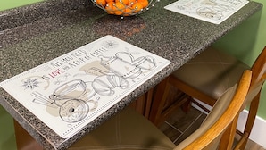 A kitchen counter with a fruit bowl, two placemats, and wooden cabinets.