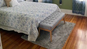 A bedroom with a bed, bench, and two windows with curtains.
