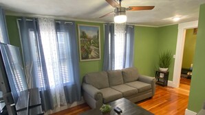 A living room with a sofa, a coffee table, a ceiling fan, and a painting on the wall.
