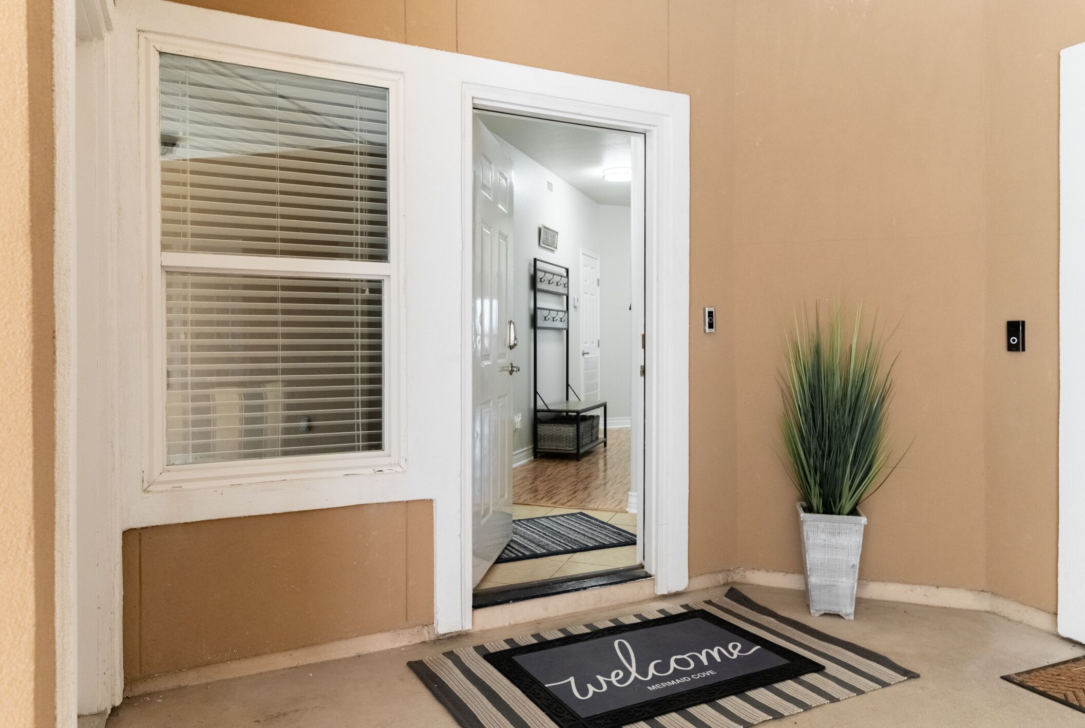 A front door with a 'welcome' mat, a potted plant, and a hallway leading inside.