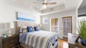 A bedroom with a bed, nightstands, a ceiling fan, a painting, and a door with blinds.