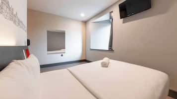 A hotel room with a bed, a flat-screen TV, a wall-mounted mirror, and a wall art piece.
