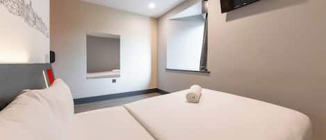 A hotel room with a bed, a flat-screen TV, a wall-mounted mirror, and a wall art piece.