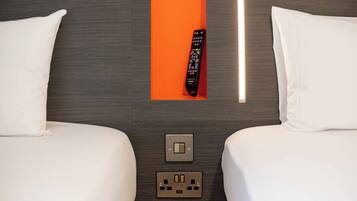 Habitación de hotel con dos camas, un control remoto, un interruptor de luz y un enchufe.