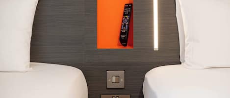 Quarto de hotel com duas camas, um controle remoto, um interruptor de luz e uma tomada.