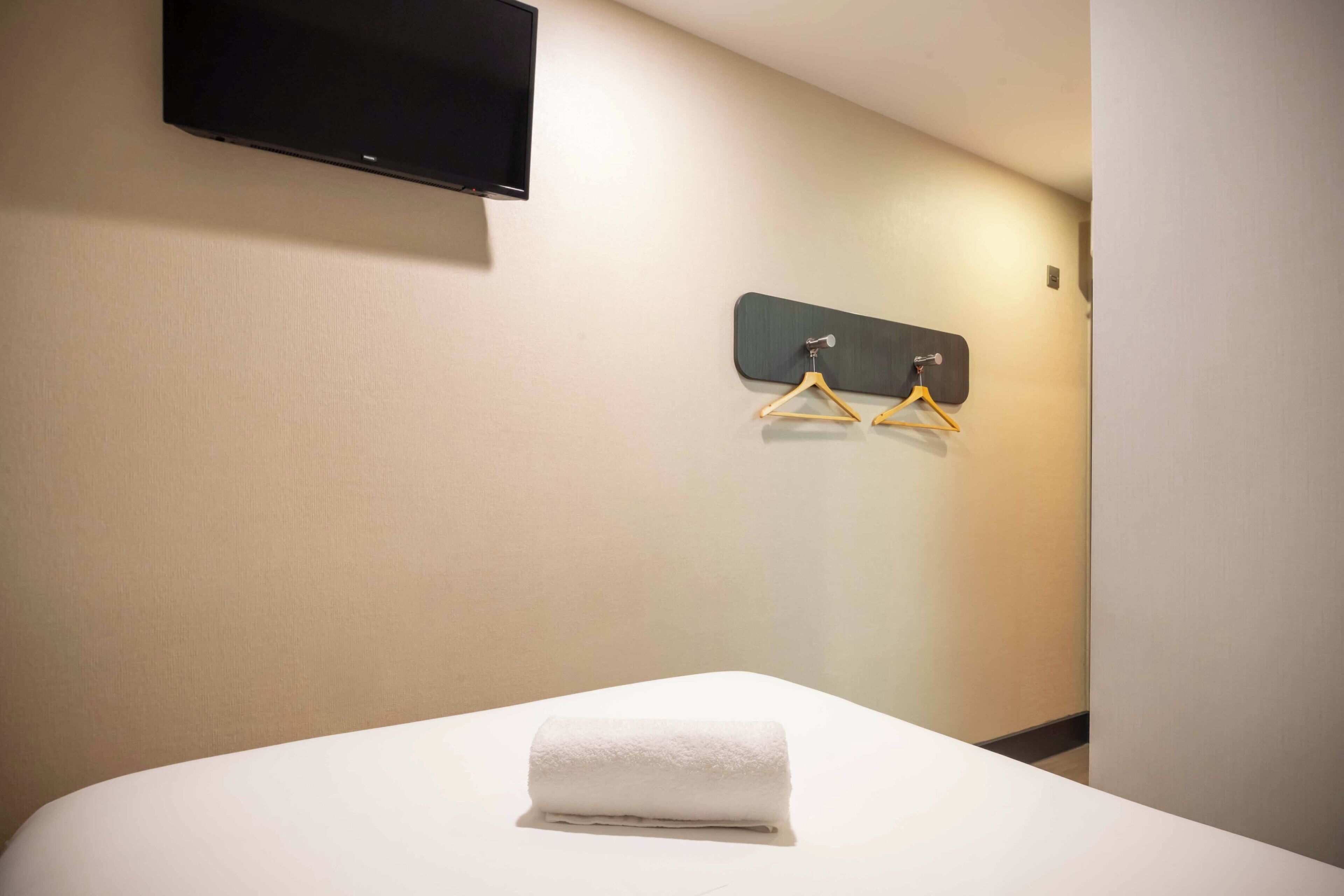 A hotel room with a bed, a flat-screen TV mounted on the wall, and two wooden hangers on a wall-mounted rack.