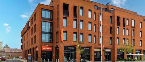 A modern brick building with multiple floors, featuring storefronts for 'easyHotel' and 'Terzetto.'