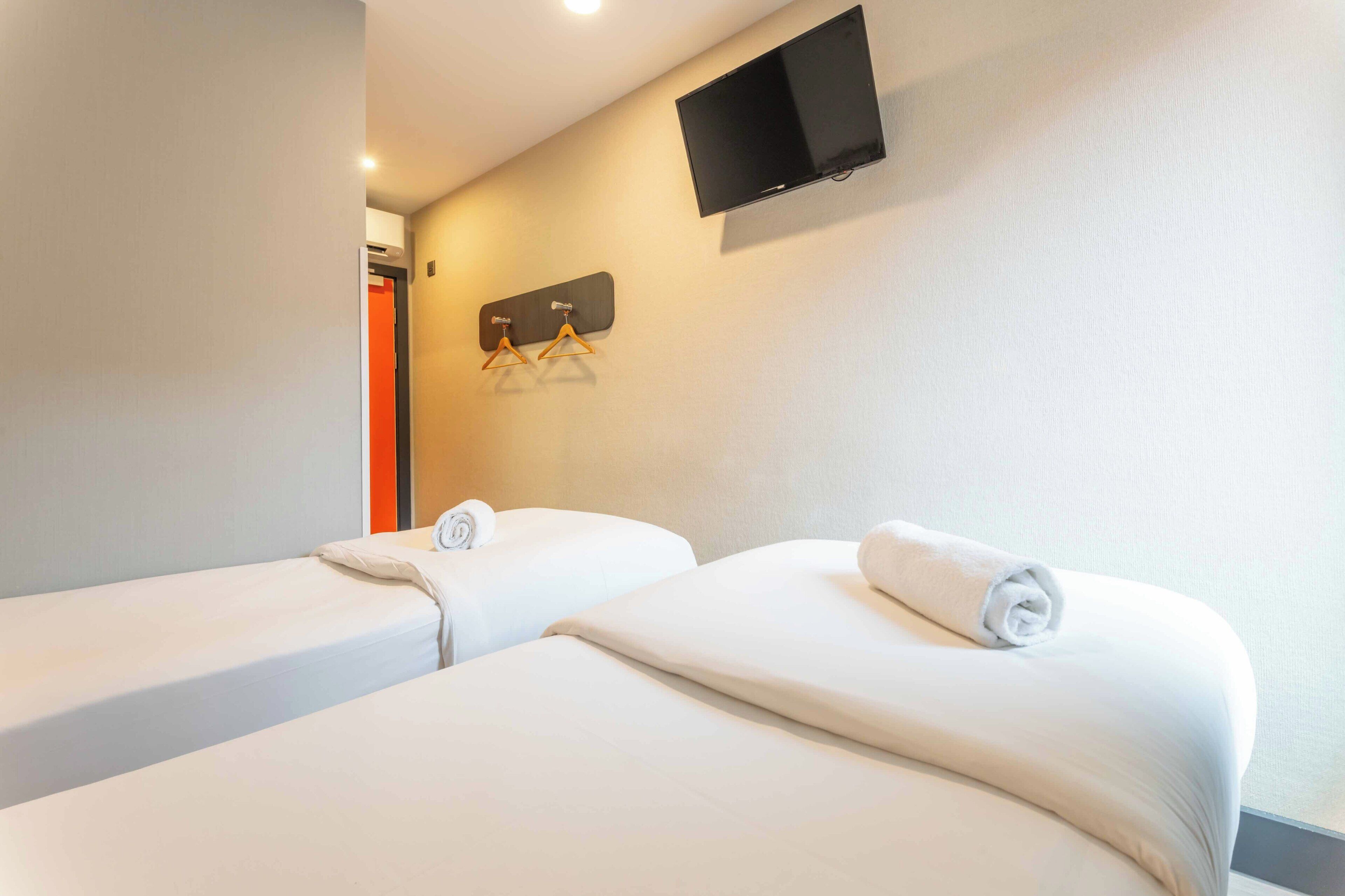 A hotel room with two beds, a flat-screen TV mounted on the wall, and a coat rack with hangers.