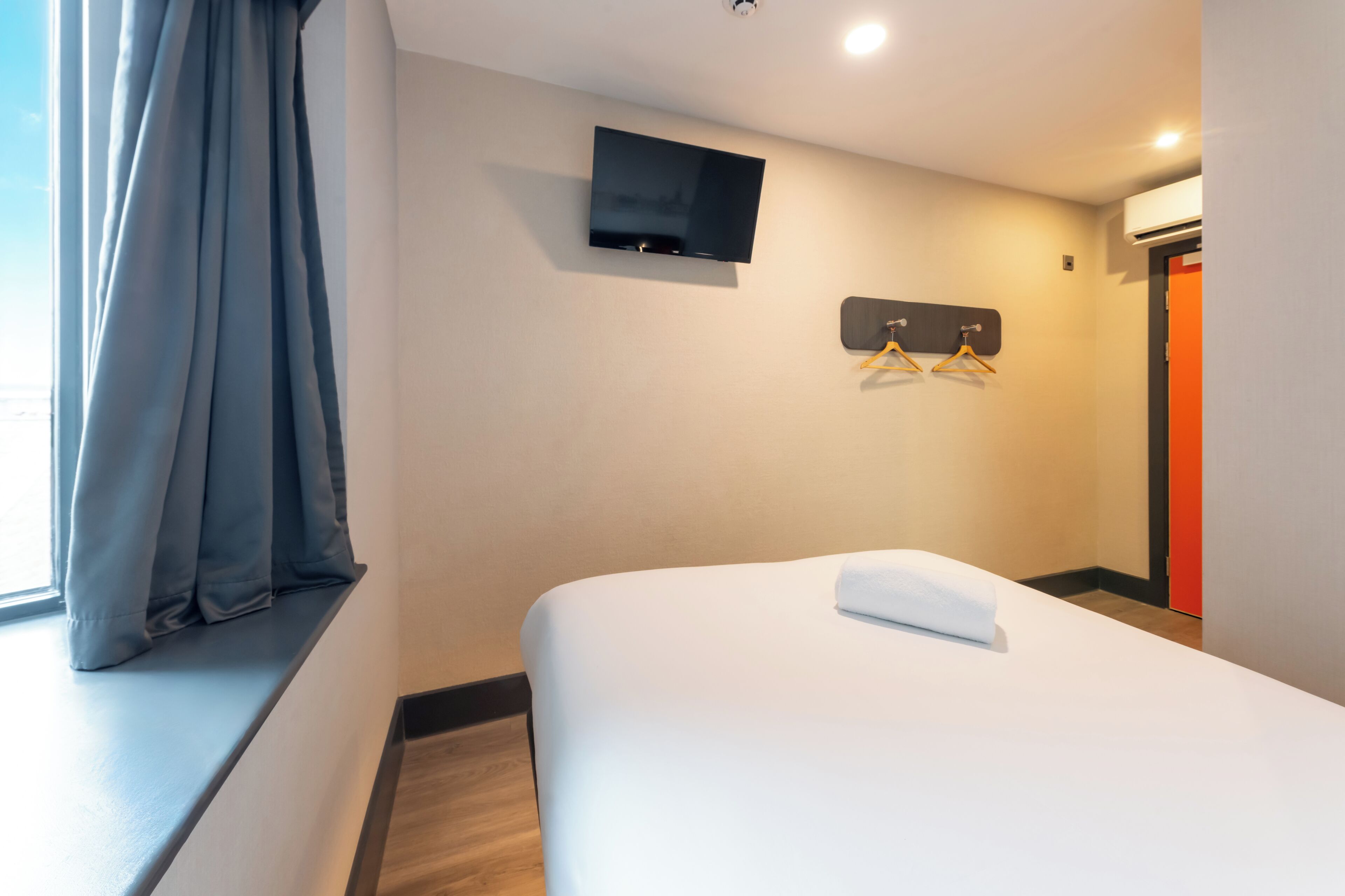 A hotel room with a bed, a TV mounted on the wall, and a coat rack with hangers.