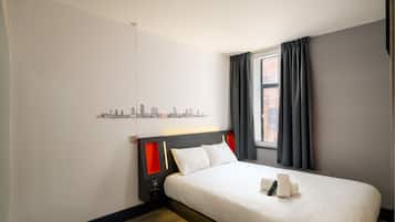 Een hotelkamer met een bed, stadsdecoratie aan de muur, een raam met gordijnen en uitzicht op de stad.