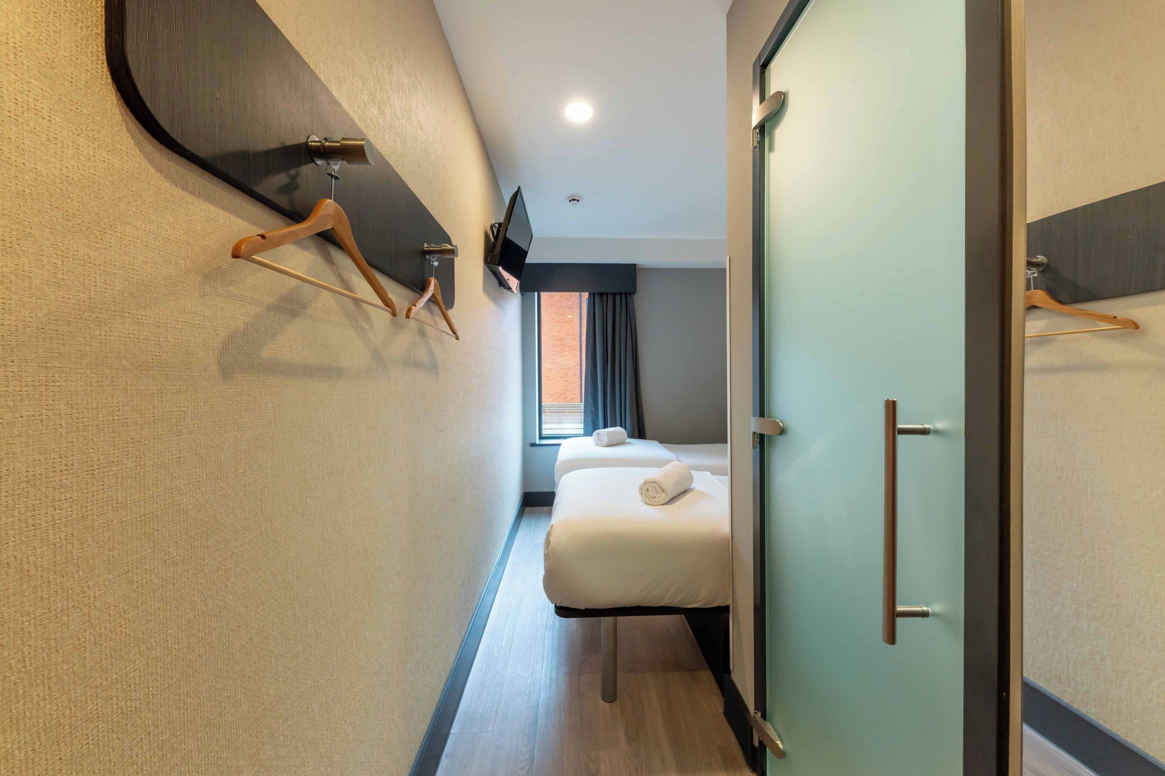 A narrow hotel corridor with a bed, a television, and a wardrobe.