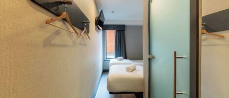 A narrow hotel corridor with a bed, a television, and a wardrobe.