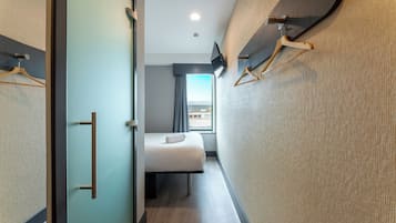 Habitación de hotel con cama, televisión, ventana con vistas y puerta con perchero.