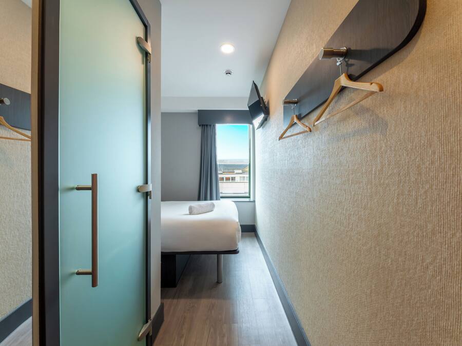 Habitación de hotel con cama, televisión, ventana con vistas y puerta con perchero.