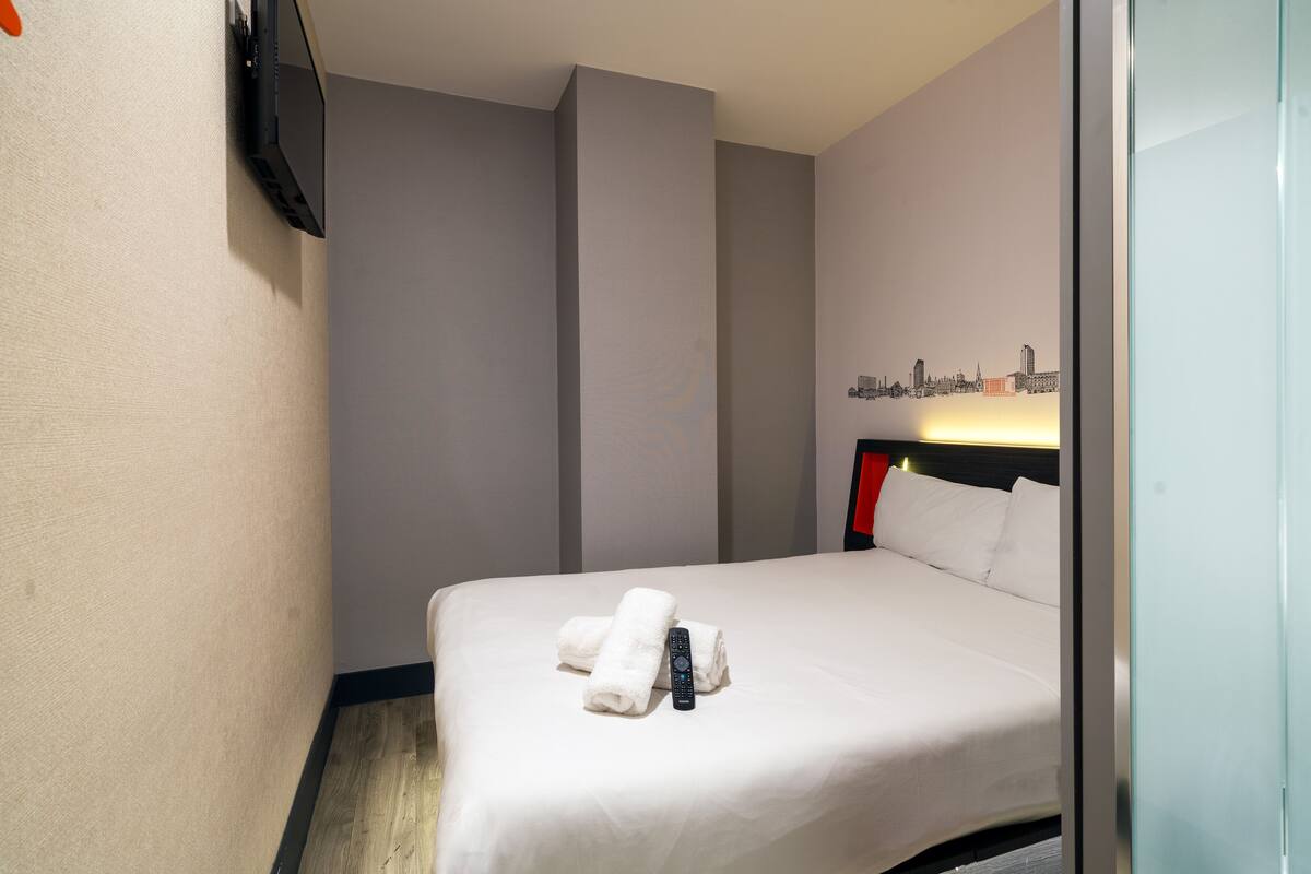 Une chambre d’hôtel avec un lit, des serviettes blanches, une télécommande et une décoration murale représentant un paysage urbain.