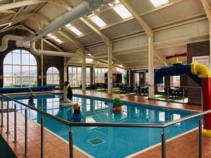 Une piscine intérieure dotée d’un haut plafond, de grandes fenêtres et de panneaux d’affichage indiquant les consignes de sécurité.