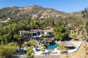 A resort with a pool, palm trees, and a mountainous backdrop.