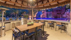 Een buitenkeuken met een houten tafel en stoelen, een ingebouwde barbecue en een achtergrond van een stenen waterval.