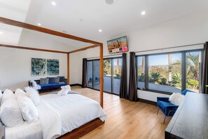 A modern bedroom with a large bed, a blue sofa, and a view of the outdoors through large windows.