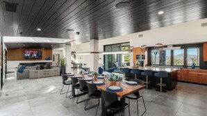 Een moderne keuken met een groot eiland, een eetgedeelte met ronde tafels, en een aan de muur bevestigde televisie.