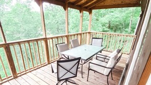 A wooden deck with a table and chairs, surrounded by a wooden railing, overlooking a forested area. - The Cabin on Current River with Private Gravel Bar!! (Van Buren)