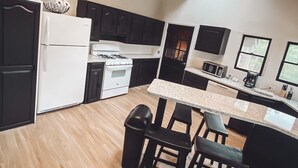 A modern kitchen with dark cabinets, a white refrigerator, a stove, and a dining area with a table and chairs. - The Cabin on Current River with Private Gravel Bar!! (Van Buren)