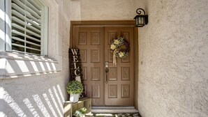 A brown door with a 'WELCOME' sign, a potted plant, and a wall-mounted light fixture. - Quiet Desert Oasis on Golf Course w/ Heated Pool (Mesa)