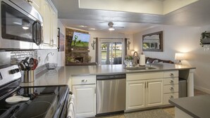 A modern kitchen with stainless steel appliances, a central island with a sink, and a dining area with a view of the outdoors. - Quiet Desert Oasis on Golf Course w/ Heated Pool (Mesa)