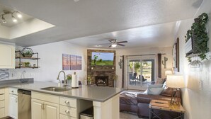 A modern kitchen with a central island, a dining area with a sofa and table, and a living room with a fireplace. - Quiet Desert Oasis on Golf Course w/ Heated Pool (Mesa)
