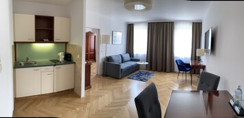 Quarto de hotel moderno com cozinha compacta, sofá, mesa de jantar e televisão.