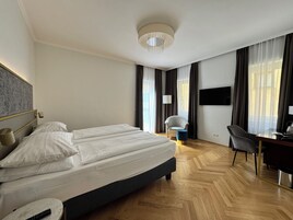Et hotelværelse med en stor seng, et skrivebord, en stol og et fjernsyn på væggen.