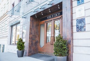 L’entrée d’un hôtel, avec une porte en bois, deux plantes en pot et une enseigne indiquant qu’il s’agit du cinquième bâtiment de la rue.