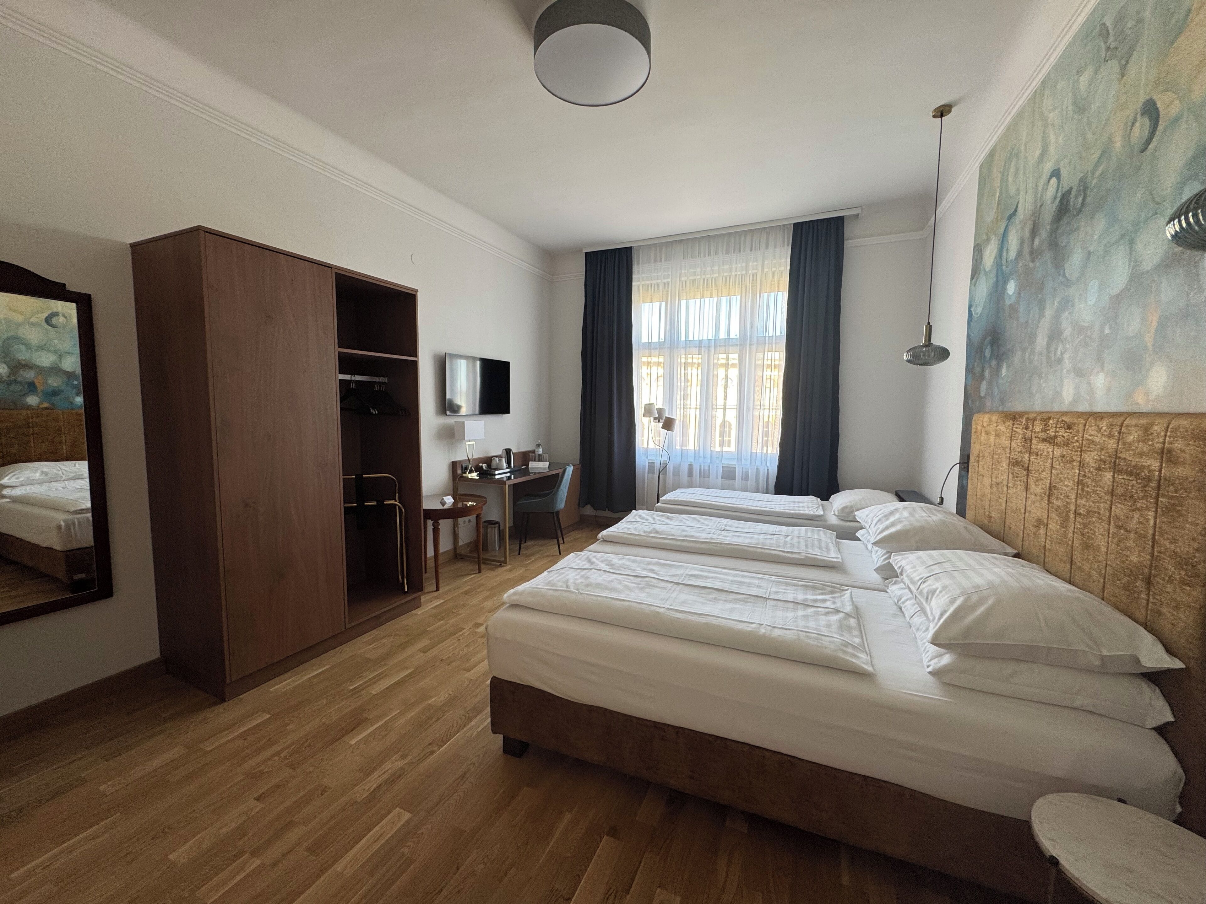 Quarto de hotel com uma cama grande, uma escrivaninha, um guarda-roupa, uma televisão e um quadro na parede.