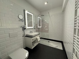 A modern bathroom with white subway tiles, a black floor, a white sink, a toilet, a glass shower enclosure, and a towel rack.